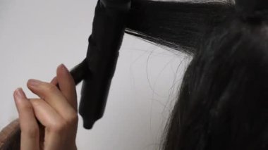 Saç stilisti, uzun kıvırcık, saç maşalı, elleri kıvırcık, elleri kapalı, salon aletleri görünür, odaklanmış teknikleri var.