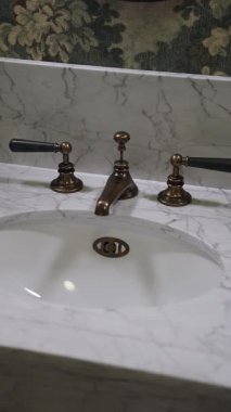 Mermer banyo lavabosu eski musluk ve çiçek duvar kağıdı fon, porselen leğen, pirinç tutamaklar ve cilalı tezgah..
