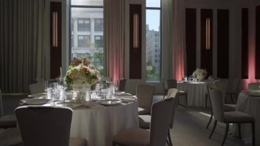 Yuvarlak Masalar Çiçek süslemeleri ve Uzun Pencere 'den dökülen Doğal Işık Ahşap Panelli Modern Ziyafet Odası