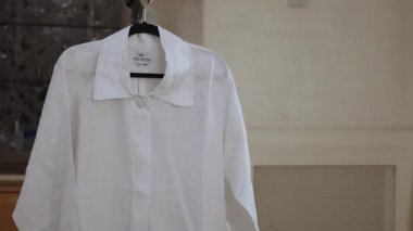 NEW YORK, ABD - 4 Ekim 2025: Hangar Tarafsız Duvarında Beyaz Gömlek, Pamuk Kumaş Görünür, Klasik Tasma ve Düğme Plaketi, Siyah Askı Silueti, Yumuşak Doğal Açık