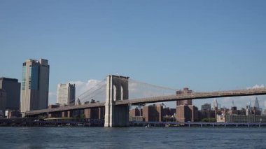 NEW YORK, ABD - 2 Ekim 2025: Brooklyn Köprüsü East River Skyline 'ı geçiyor. Rıhtımda Mimarlık, Feribot Trafiği, Yansıtıcı Su, Açık Mavi Gökyüzü,