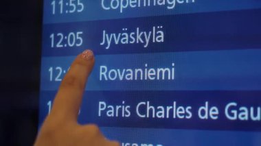 Jyvaskyla, Moskova ve Bükreş 'in kalkış saatlerini mavi ışıklı arka planı olan bir havaalanı terminalinde gösteren uçuş takvimine parmak dokunuyor