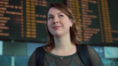 Kafkas kadın gezgin havaalanındaki uçuş bilgilerine bakar, kalkış saatleri ve varış yerleri yoğun bir seyahat ortamında görünür.