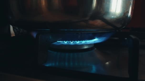 Старая газовая горелка с голубым пламенем крупным планом на кухне и кастрюлей сверху в темноте.. — стоковое видео