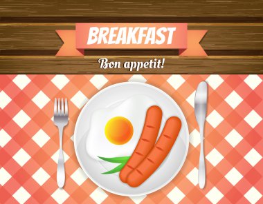 Kahvaltı Masası. Sahanda yumurta, sosis bir tabak, çatal ve bıçak. Ahşap masa üzerinde kırmızı kareli masa örtüsü