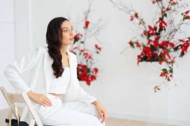 Beyaz pantolonlu orjinal gelin, geleneksel bir düğün töreni için çiçek desenli alışılmadık bir kompozisyonun arka planında poz veriyor.