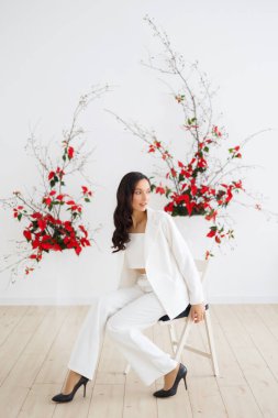 Beyaz pantolonlu orjinal gelin, özel bir düğün töreni için çiçek desenli alışılmadık bir kompozisyonun arka planında poz veriyor.