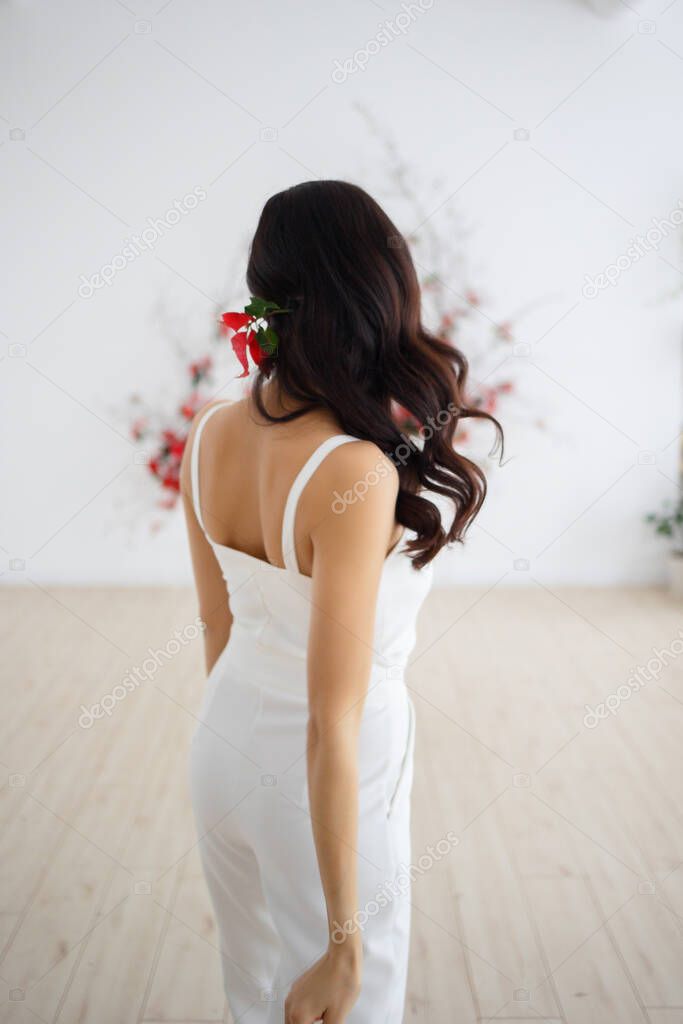 The back of a girl in a white suit on the background of a flower arrangement of a wedding arch. The girl goes to the wedding ceremony.