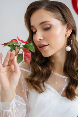 Güzel, genç bir gelin elinde kırmızı bir çiçek tutuyor. Düğün dekorunda kırmızı. Duygular ve sevinç.