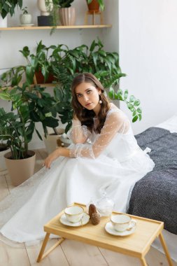 Beyaz gelinlikli esmer gelin nihai gri yatakta oturuyor. Yılın renkleri.