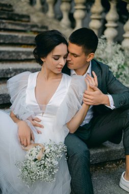 Parktaki merdivenlerde beyaz çingene çiçekleriyle süslenmiş muhteşem bir çiftin portresi. Tropik bir bahçede gün batımında yeni evliler..