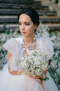 Çiçeklerle süslenmiş bir buket çiçekle şık bir gelin. Karısının omuzlarında fırfırlar olan beyaz gelinlik..