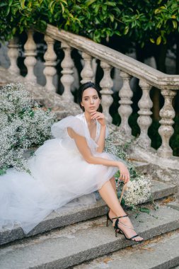 Çiçeklerle süslenmiş bir buket çiçekle şık bir gelin. Karısının omuzlarında fırfırlar olan beyaz gelinlik..