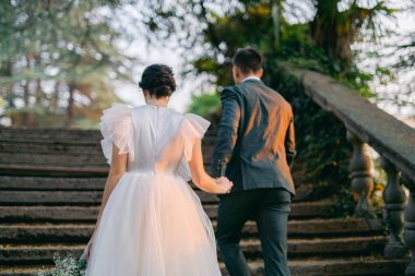 Gelinlik giymiş güzel bir çift tropik bahçenin arasında merdivenleri tırmanıyor..