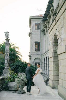 Muhteşem bahçe manzaralı bir arka planda şık bir çift yürüyüşü. Moda bir gelinlik içinde genç ve şık bir gelin ve iki kişilik bir düğünde yakışıklı bir damat..