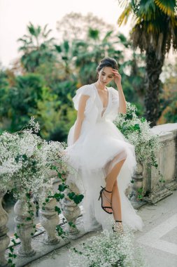 Düğün töreni için kemerin arka planında duran bir buket çiçekle şık bir gelin. Karısının omuzlarında fırfırlar olan beyaz gelinlik..