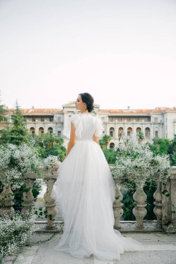 Çiçek ve dekorla düğün kemerinin önünde güzel bir gelin. Buket ellerde ve detaylarda. Kız mutlu, gülümsüyor ve dans ediyor. Modern tarzda bir gelinlik hayal et.