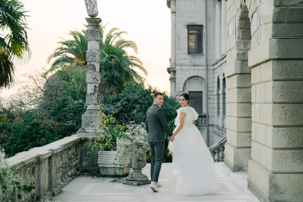 stylish wedding couple strolls against a backdrop of magnificent garden views. A young and stylish bride in a trendy wedding dress and a handsome groom at a wedding for two.