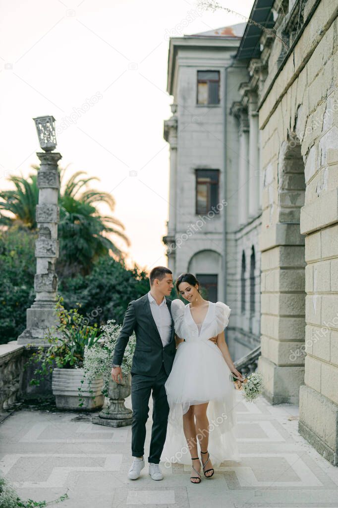 stylish wedding couple strolls against a backdrop of magnificent garden views. A young and stylish bride in a trendy wedding dress and a handsome groom at a wedding for two.