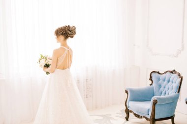 İçerde zarif ve şık bir gelinlik giymiş bir gelinin tam boy portresi. Kadın sırtüstü durur ve düğün günü kocasıyla ilk görüşmesini bekler..