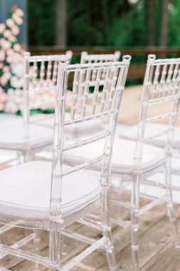Üst üste yapılan düğün töreninde şeffaf plastik sandalyeler. Konuklar için yastıklı, şeffaf plastik sandalyeler düğün kemerine karşı ayakta duruyor. Seçili odak ve bulanık arkaplan.