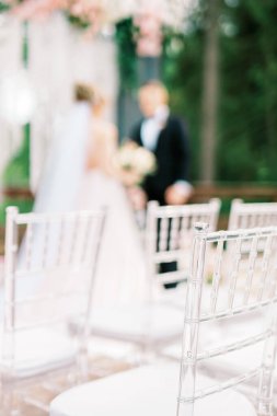 Avrupa tarzında modern bir tören. Konuklar için yastıklı, şeffaf plastik sandalyeler düğün kemerine karşı ayakta duruyor. Seçili odak ve bulanık arkaplan.
