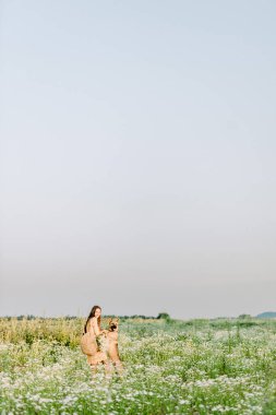 Esmer bir kız çayırda Alman çoban köpeğiyle yürüyor ve oynuyor. Arkaplanda gün batımı ve bulanık arkaplan.