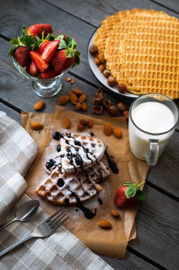 Çikolata sosu, çilek, fındık, badem, pudra şekeri ve bir bardak süt ile fırın kağıt üzerinde ev yapımı Belçika waffle hizmet