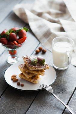 Ev yapımı Belçika waffle çilek, fındık, badem, pudra şekeri ve süt beyaz tabakta servis