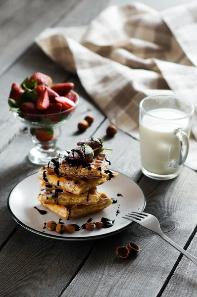 Gofres belgas caseros servidos en plato blanco con salsa de chocolate, fresa, avellanas, almendras, azúcar en polvo y vaso de leche Imágenes De Stock Sin Royalties Gratis