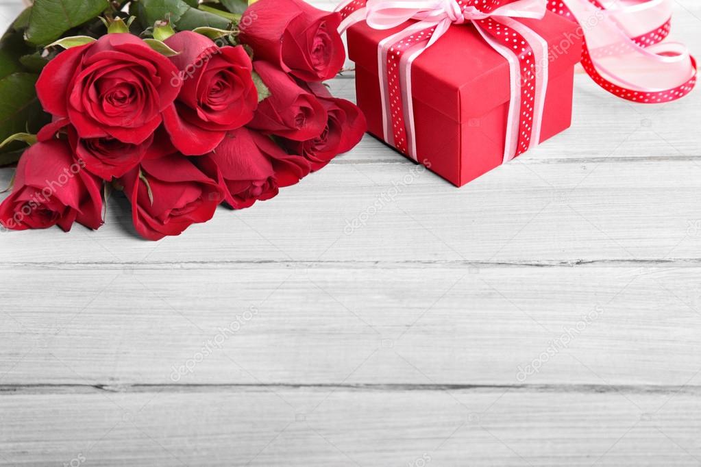 Valentine background of gift box and red roses on white wood. Sp