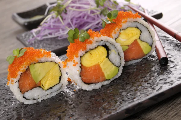 Sushi de rolo de Califórnia com caviar e pauzinhos em uma bandeja preta — Fotografia de Stock