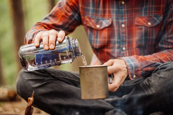 man traveler pours water from a bottle into a metal mug.