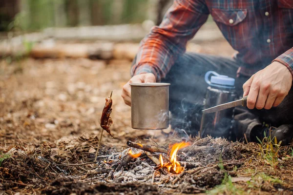 Hombre viajero manos celebración taza con agua cerca del fuego al aire libre — Foto de Stock