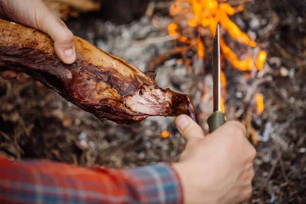 Homem a esculpir carne de coelho grelhada no acampamento da floresta. Vista superior . — Fotografia de Stock