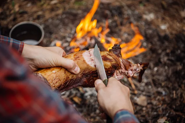 Man snijwerk gegrilde konijn vlees in forest camp. Bovenaanzicht. — Stockfoto