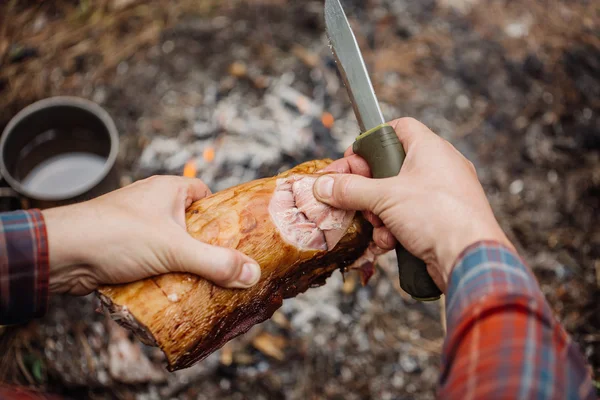 Férfi carving sült nyúl hús erdő kempingezik. Szemközti nézet. — Stock Fotó