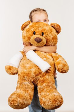 Kırık kol genç kızla bir yumuşak oyuncak ayı saklanıyor.