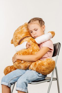 Kırık kol ile genç üzgün kız bir yumuşak oyuncak ayı tutuyor.