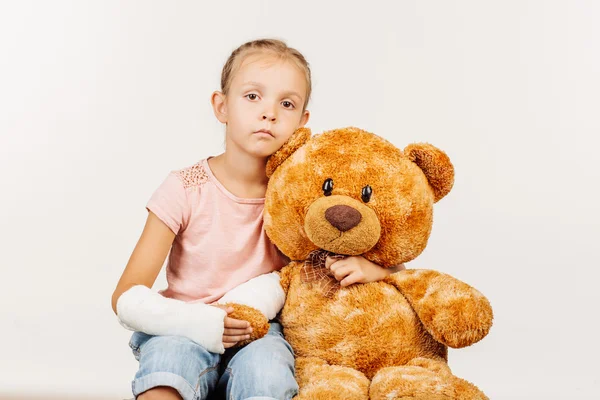 Cute little girl with broken arm in the gypsum with teddy bear