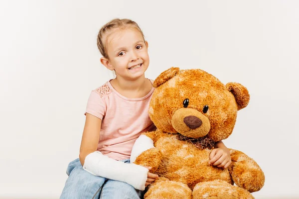 Молодая девушка со сломанной рукой держит мягкого игрушечного медведя . — стоковое фото