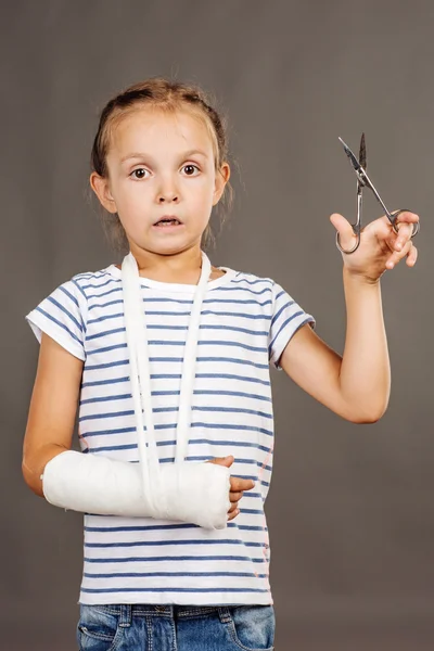 Menina assustada nova com braço quebrado está de pé sobre o fundo cinza — Fotografia de Stock