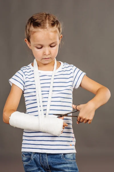 Ernstes junges Mädchen mit gebrochenem Arm steht auf dem grauen Hintergrund — Stockfoto
