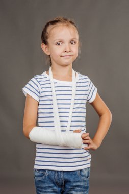 Kırık kol ile gülümseyen kız gri arka plan üzerinde duruyor.