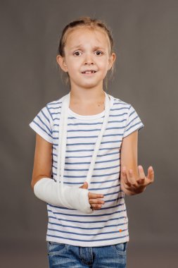 Kırık kol ile şaşırmış ve üzgün kız gri arka plan üzerinde duruyor