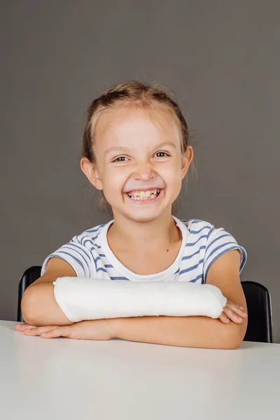 Młoda dziewczyna szczęśliwy ze złamaną rękę siedzi przy stole. Medycyna — Zdjęcie stockowe
