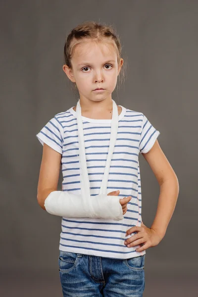 Menina entediada com o braço quebrado está de pé sobre o fundo cinza . — Fotografia de Stock