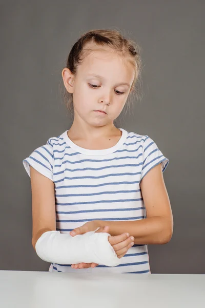 Menina com braço quebrado está de pé perto da mesa . — Fotografia de Stock