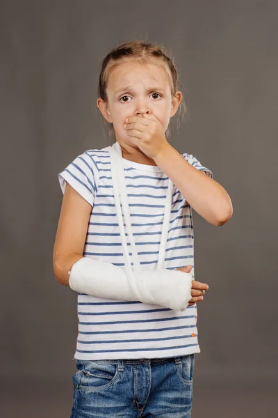 Distressed girl with broken arm is standing on the gray background