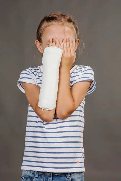 Smutna dziewczyna ze złamaną rękę stoi na szarym tle. — Zdjęcie stockowe